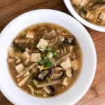 overhead view of hot and sour soup in white bowl on wood cutting board