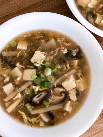 overhead view of hot and sour soup in white bowl on wood cutting board