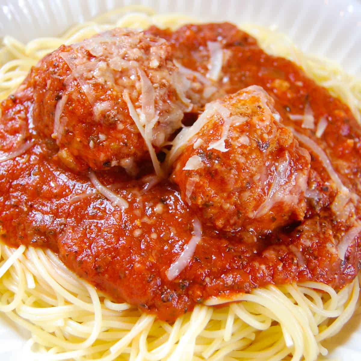 spaghetti with red sauce and two meatballs on white plate