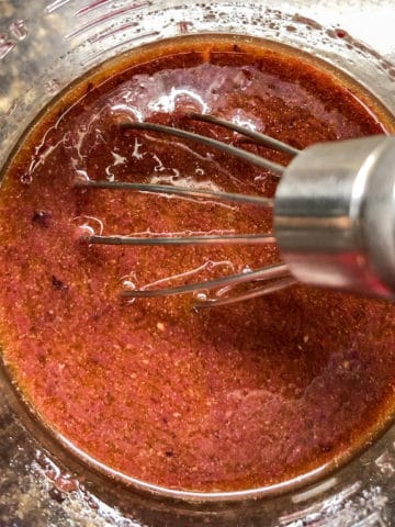 overhead view of kalamata vinaigrette in measuring cup with whisk