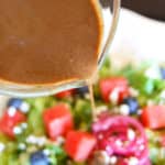 balsamic vinaigrette drizzled out of glass measuring up onto watermelon and blueberry salad
