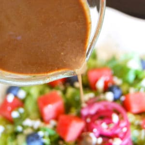 balsamic vinaigrette drizzled out of glass measuring up onto watermelon and blueberry salad