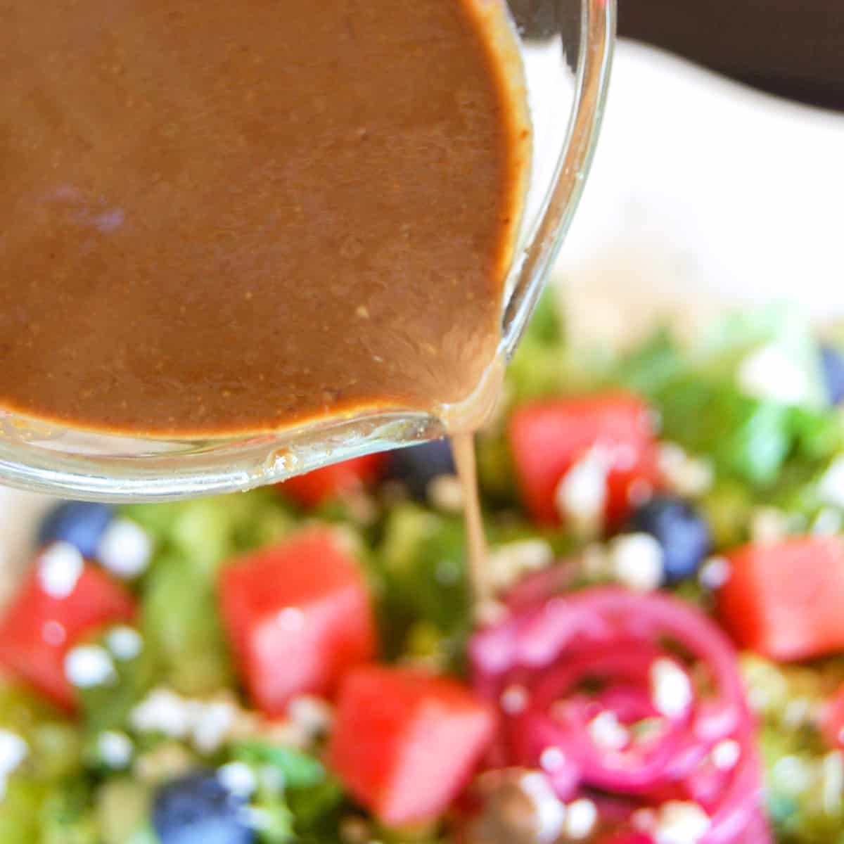 balsamic vinaigrette drizzled out of glass measuring up onto watermelon and blueberry salad