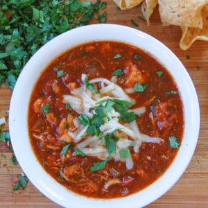 white bowl of chicken tortilla soup topped with melting grated monterey jack cheese