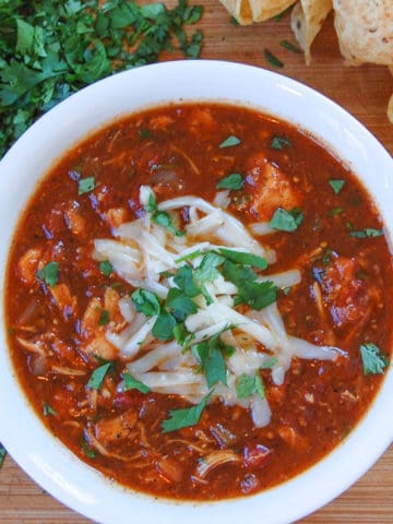 white bowl of chicken tortilla soup topped with melting grated monterey jack cheese