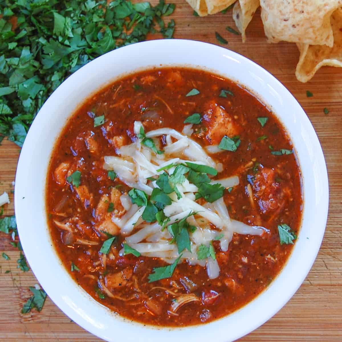 white bowl of chicken tortilla soup topped with melting grated monterey jack cheese
