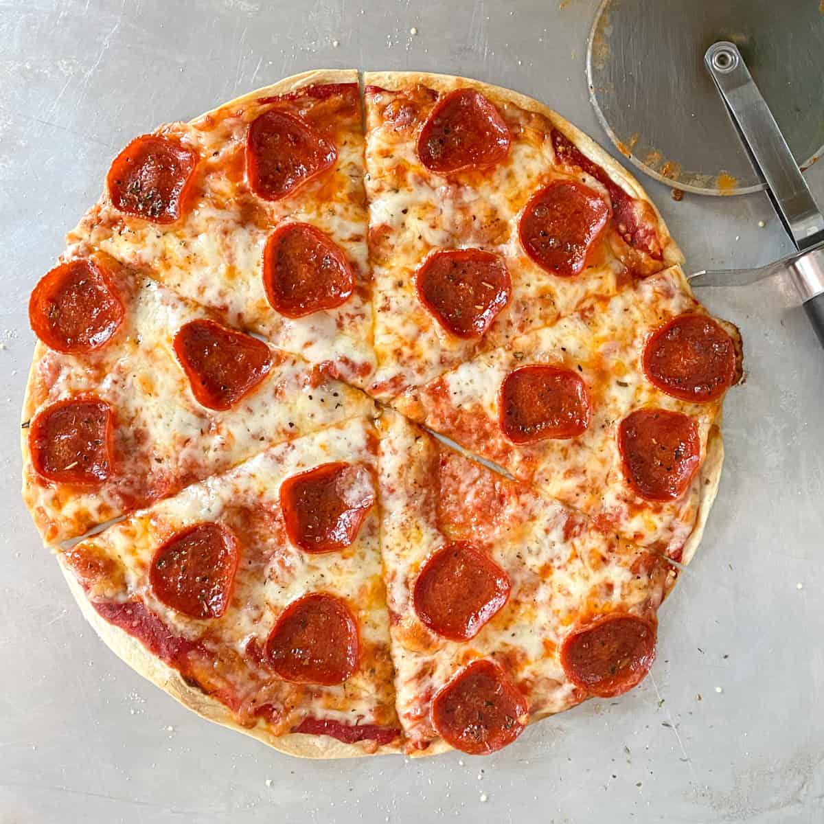 tortilla pizza with pepperoni and cheese on metal baking sheet
