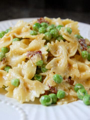 pasta carbonara with bowtie pasta, peas, and chopped bacon on white plate