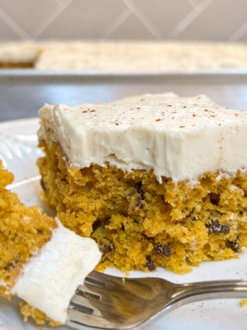 piece of pumpkin cake with creamy white icing on plate with fork