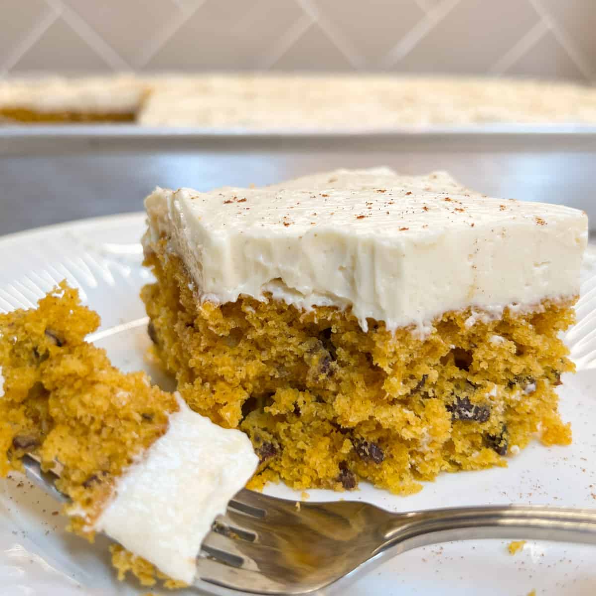 piece of pumpkin cake with creamy white icing on plate with fork