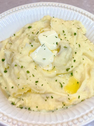 white bowl containing mashed potatoes with two pats of butter melting on top and sprinkled with chopped parsley