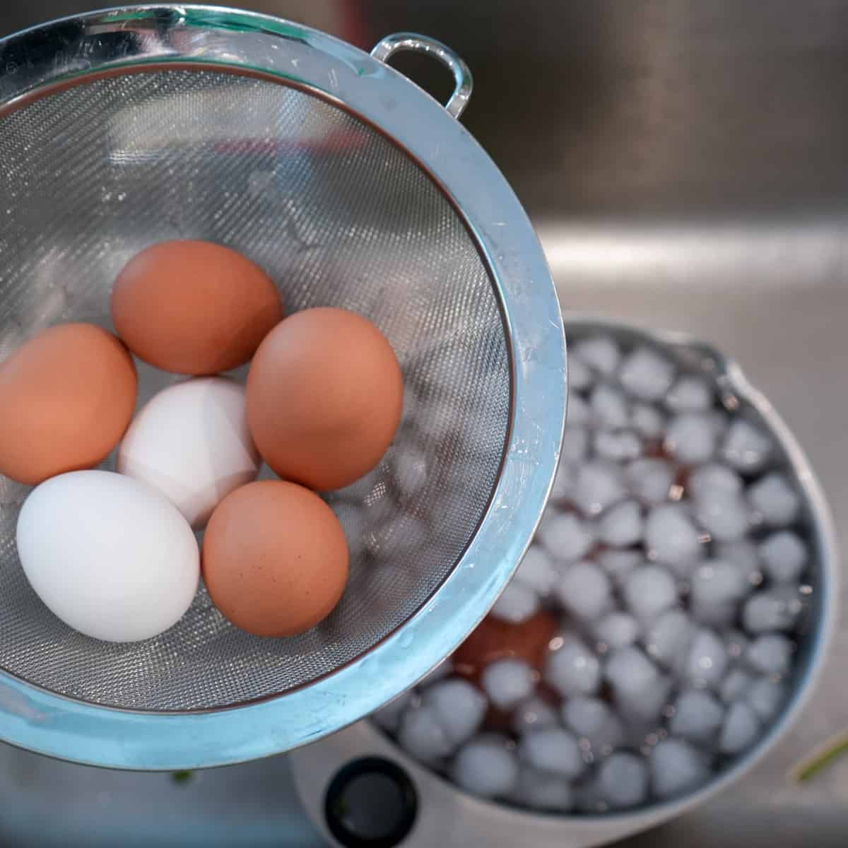 red skinned potatoes in bowl of ice water in background; six eggs in 8-inch strainer in foreground