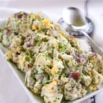 red-skinned potato salad with hard boiled eggs sprinkled with chopped parsley on a rectangular platter