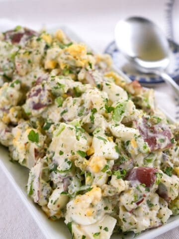 red-skinned potato salad with hard boiled eggs sprinkled with chopped parsley on a rectangular platter